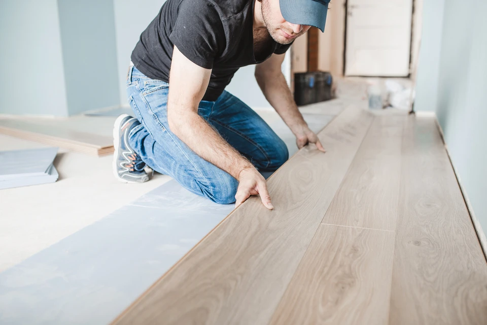 Un homme à genoux installe du parquet flottant dans une pièce en rénovation