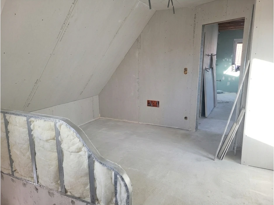 Ouvrier en bâtiment équipé d'un casque de sécurité jaune travaille à genoux sur un chantier intérieur, mesurant et positionnant des plaques de plâtre