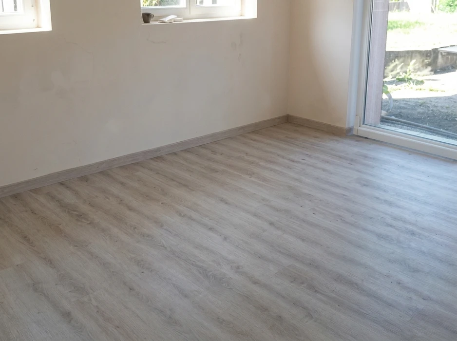 Pièce vide avec sol en parquet stratifié gris clair, style chêne blanchi, posé en lames parallèles avec plinthes assorties