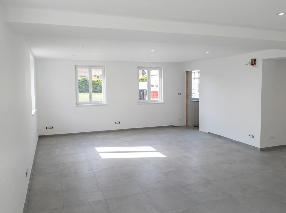 Pièce vide en fin de chantier, murs blancs enduits, sol en carrelage grès cérame gris 60x60, faux plafond avec spots encastrés LED
