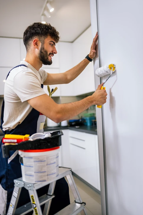 Peintre professionnel en combinaison grise et gants rouges appliquant de la peinture murale avec un rouleau sur mur texturé beige