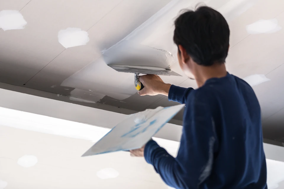 Un artisan installe un plafond suspendu dans un intérieur blanc