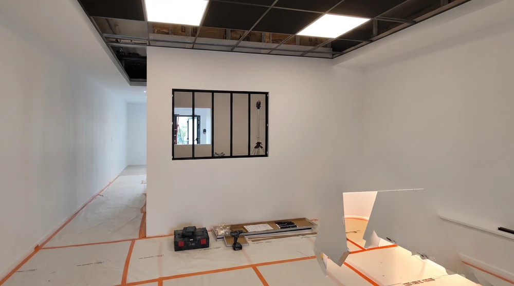 Ouvrier en tenue de travail debout sur un escabeau rouge, installant une ossature métallique en profilés d'acier galvanisé pour cloisons en plaques de plâtre