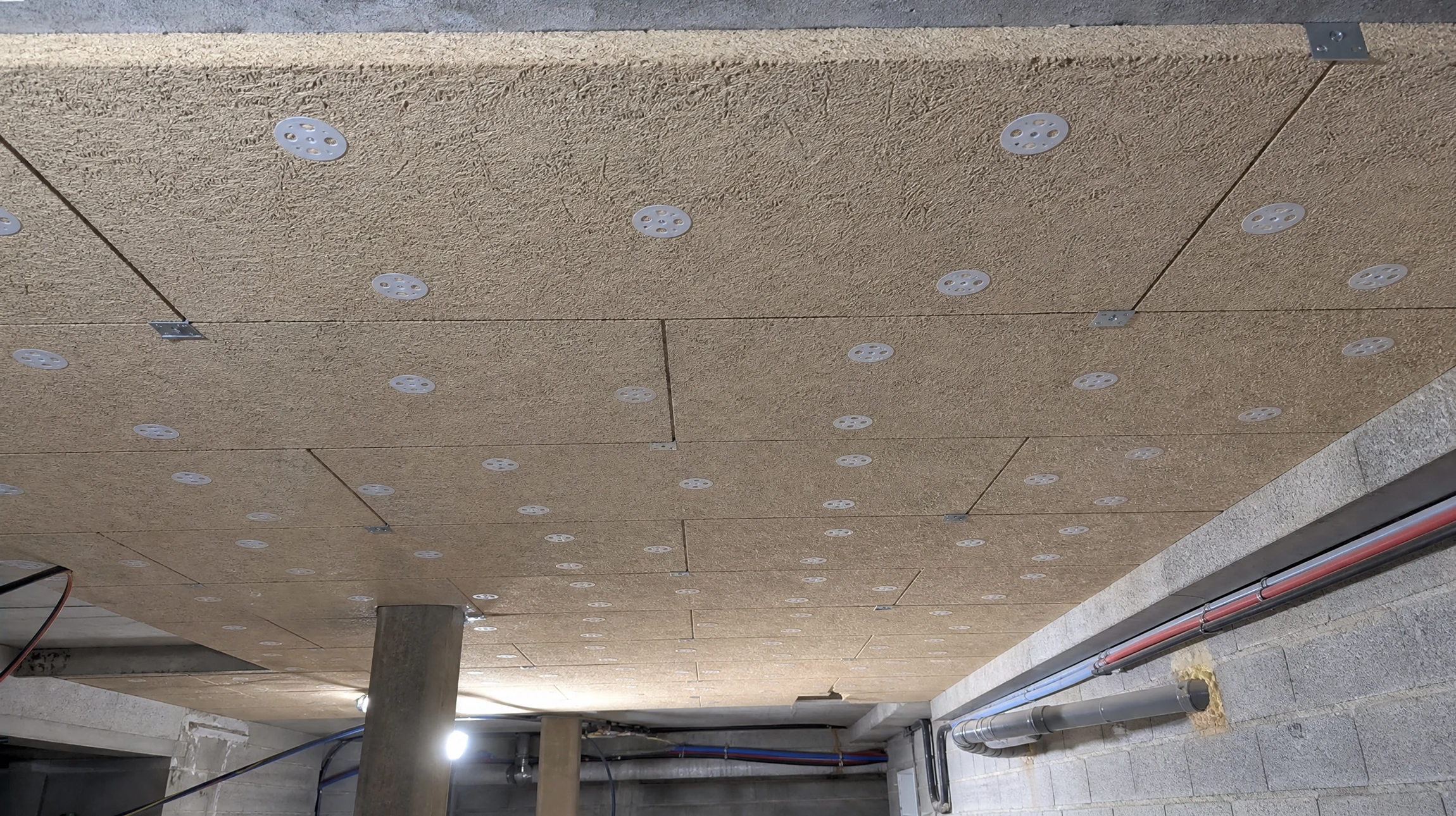 Ouvrier en bâtiment installant isolation thermique, agenouillé sur plancher bois, utilisant perceuse électrique sur panneau isolant laine de roche
